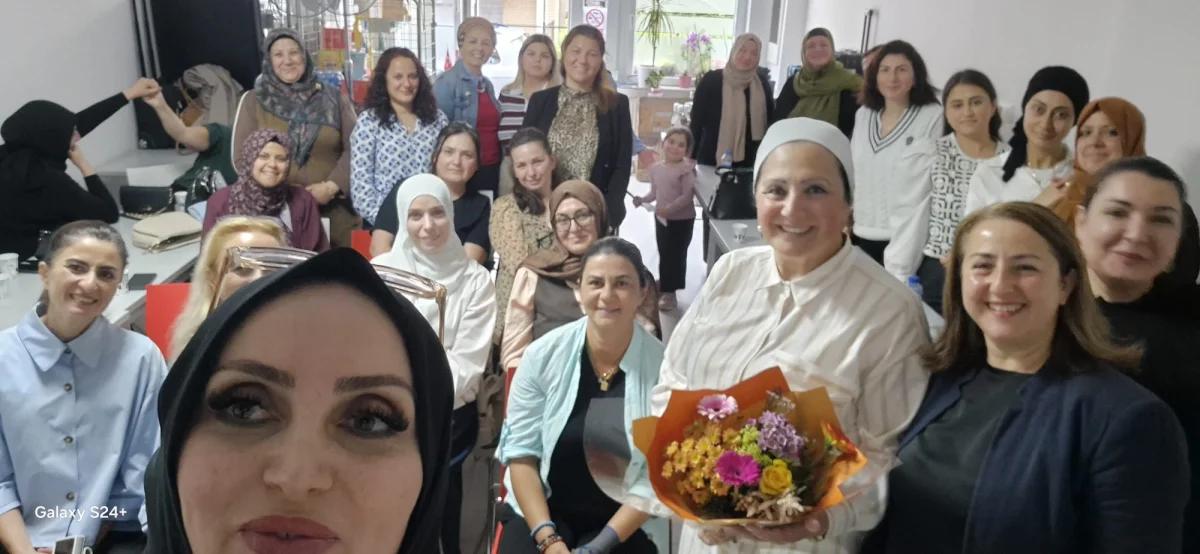 Bir grup kadın, konferans alanında gülümseyerek poz veriyor; ön planda çiçek buketi tutan bir kadın var.