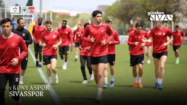 Kırmızı formalar giyen futbolcular, çim sahada koşu antrenmanı yaparken görülüyor.