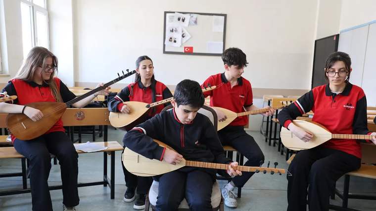 Bir sınıfta oturan beş öğrenci, ellerindeki bağlamaları çalarken görülüyor.