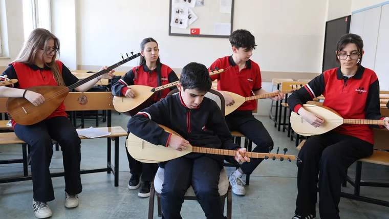 Bir sınıfta oturan beş öğrenci, ellerindeki bağlamaları çalarken görülüyor.