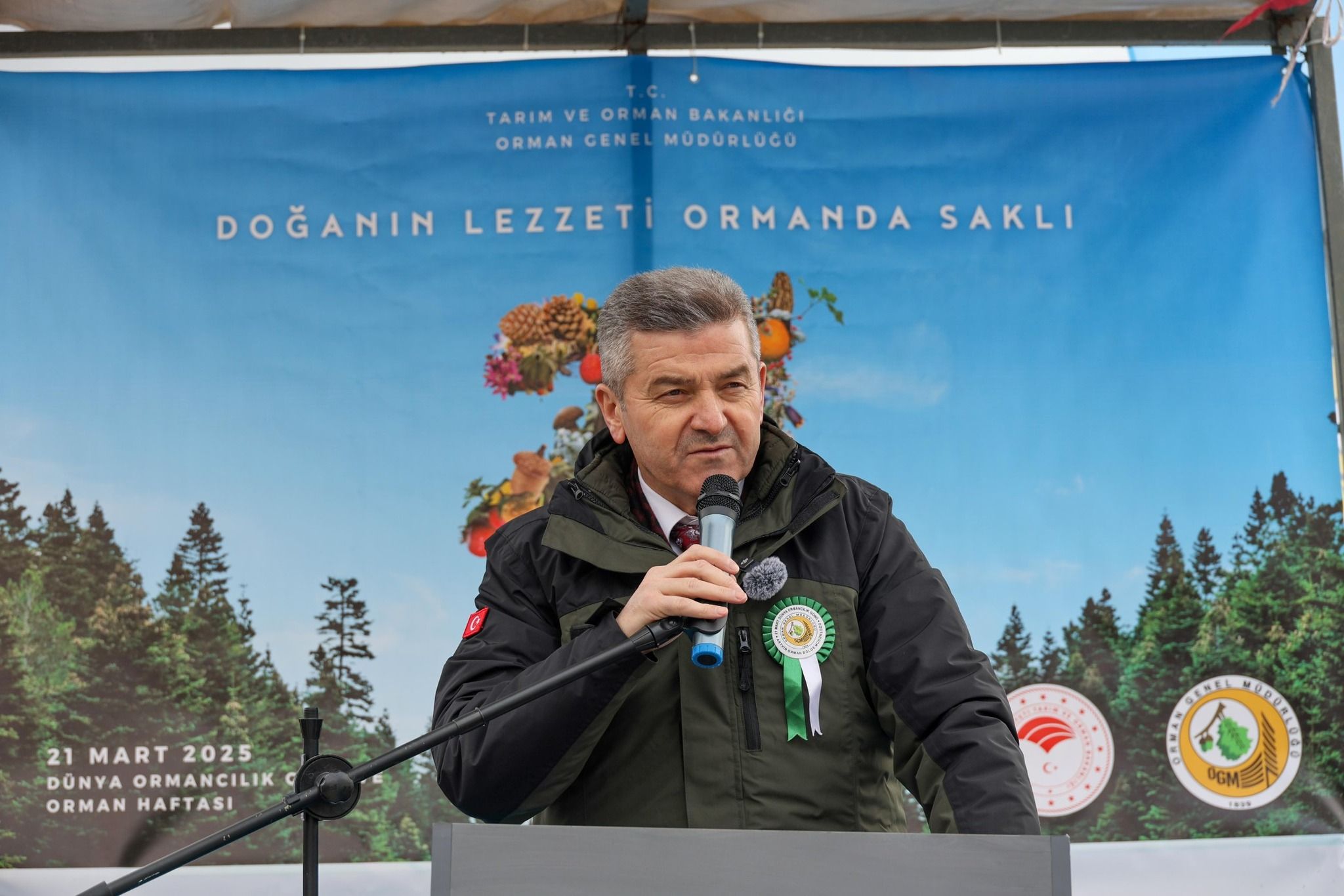 Mikrofonla kürsüde konuşan bir kişi, Orman Genel Müdürlüğü yazılı mavi pankartın önünde duruyor.