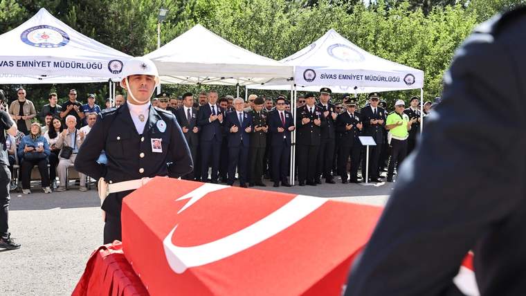 Türk bayrağına sarılı tabut, bir grup insanın önünde duruyor; arka planda çadırlar ve kalabalık var.