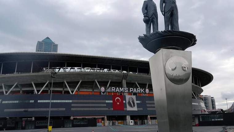 RAMS PARK önünde, üzerinde iki heykel bulunan anıt ve Türk bayrağıyla kulüp flamaları görülüyor.