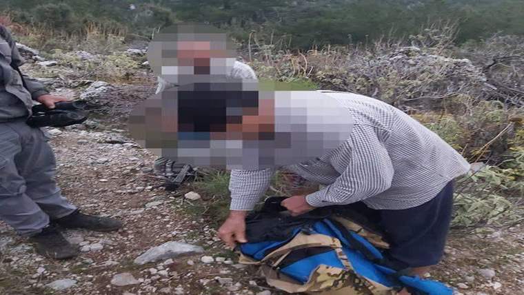 Kayalık arazide bir kişi sırt çantasını açarken, başka bir kişi yanında ayakta duruyor.
