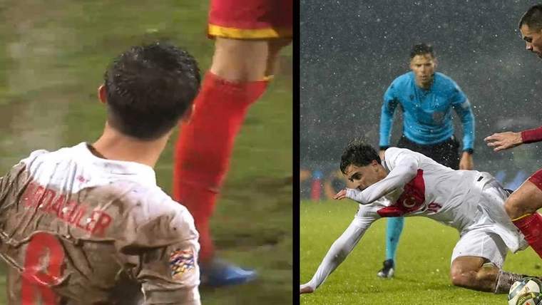 Yağmur altında futbol maçı sırasında bir oyuncu yere düşmüş, diğer oyuncu ise ona doğru yaklaşmakta.