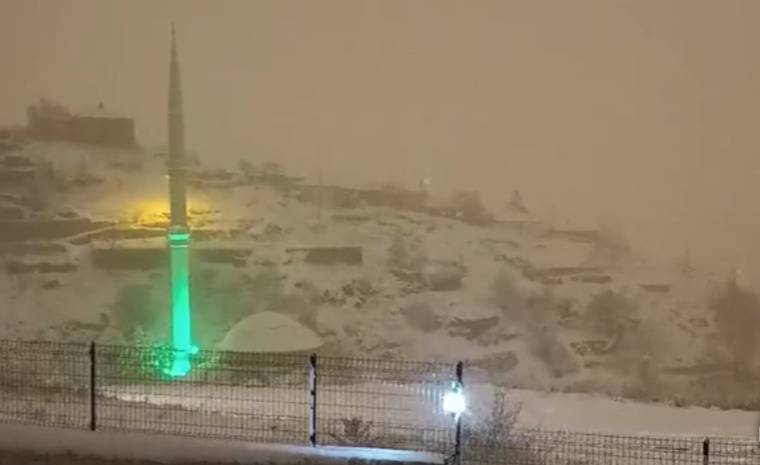 Karla kaplı bir alanın önünde, yeşil ışıkla aydınlatılmış bir minare görünmekte.
