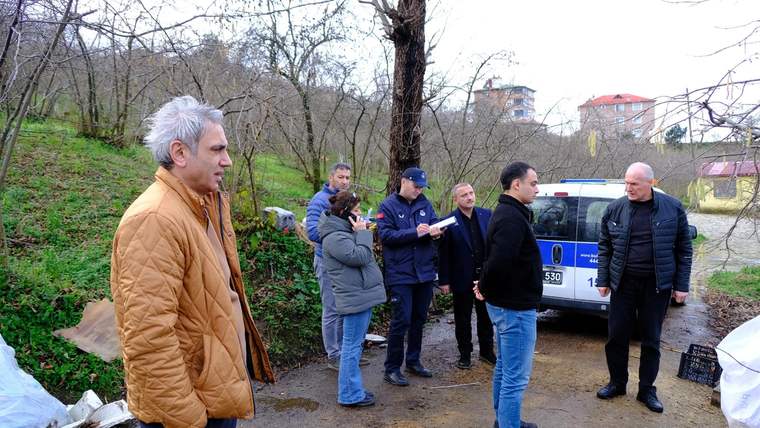 Ağaçlık alanda birkaç kişi, park halindeki üzerinde numara bulunan bir aracın yanında duruyor.