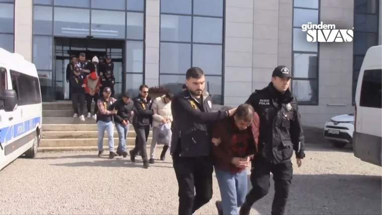 Polis ekipleri, gözaltındaki kişileri binadan çıkararak götürüyor.