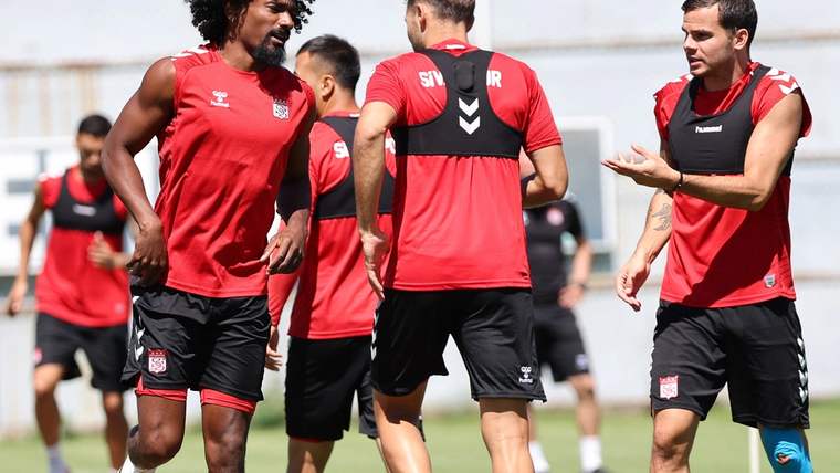 Kırmızı-siyah formalar giyen futbolcular, çim sahada antrenman sırasında birlikte yürüyor.