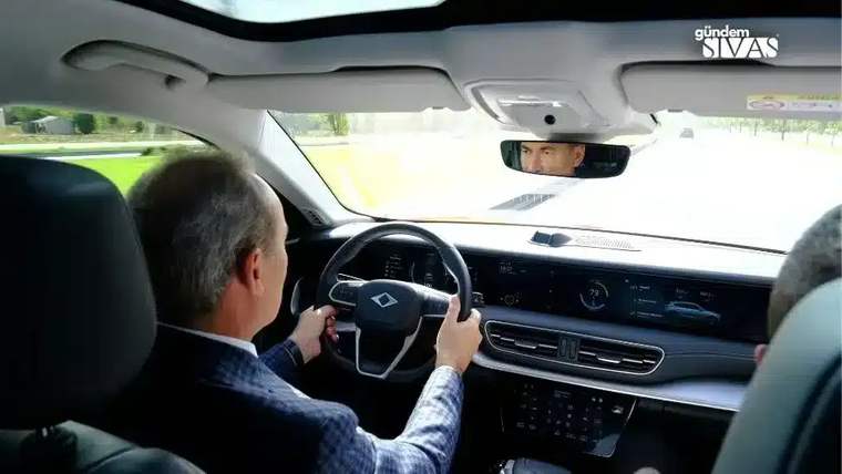 Bir kişi, TOGG marka aracın direksiyonunu tutarak sürüş yapıyor.