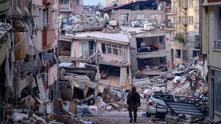 Yıkılmış bir bina ve etrafında dağılmış inşaat malzemeleri, bir kişi yıkıntıların önünde duruyor.