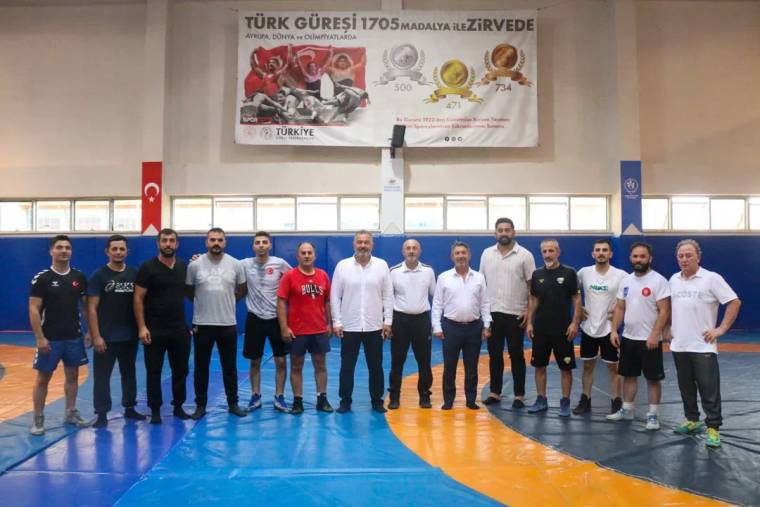 Güreş antrenörlerinin bulunduğu bir grup, spor salonunda poz veriyor.