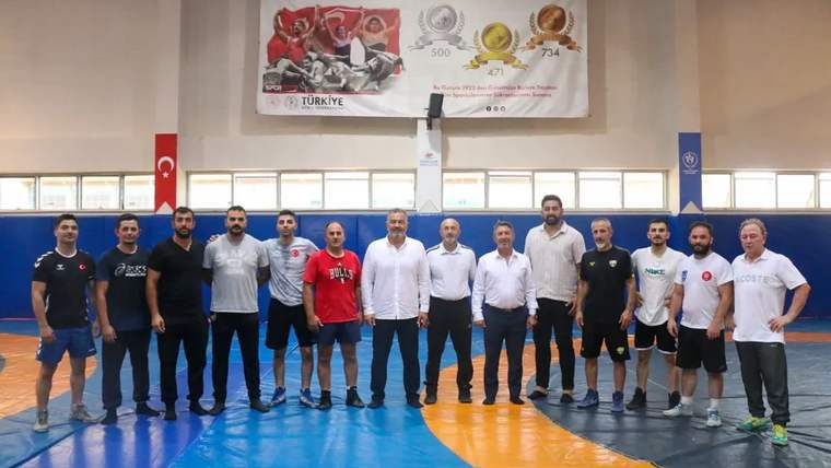 Güreş antrenörlerinin bulunduğu bir grup, spor salonunda poz veriyor.
