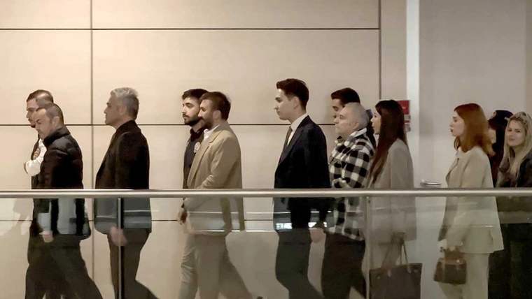 Bir grup insan, bir koridorda yürüyerek ilerliyor; bazıları resmi kıyafetler giymekte.