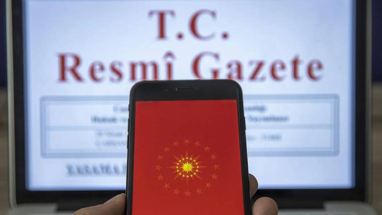 Kırmızı ekranında ay yıldızlı arma bulunan akıllı telefon, arkasındaki T.C. Resmî Gazete sayfasını kapatıyor.