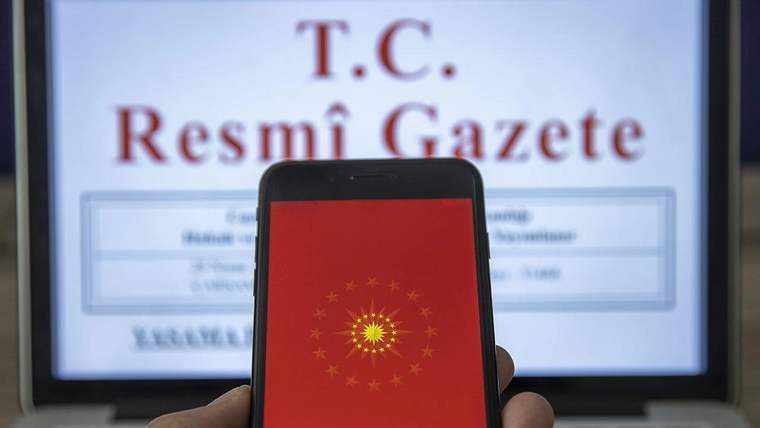 Kırmızı ekranında ay yıldızlı arma bulunan akıllı telefon, arkasındaki T.C. Resmî Gazete sayfasını kapatıyor.