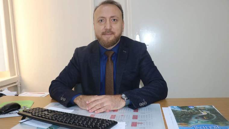 Masada oturan bir kişi, önünde bir bilgisayar klavyesi ve takvim var.