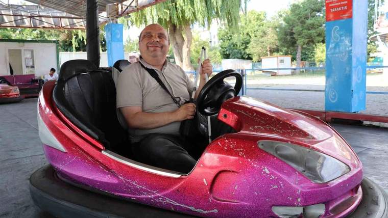 Görme engelli bir kişi, pembe bir dodgem aracında gülümseyerek oturuyor.