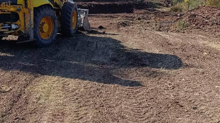 Toprak zeminde çalışan sarı bir iş makinesi, önündeki alanı düzleştirirken görülüyor.