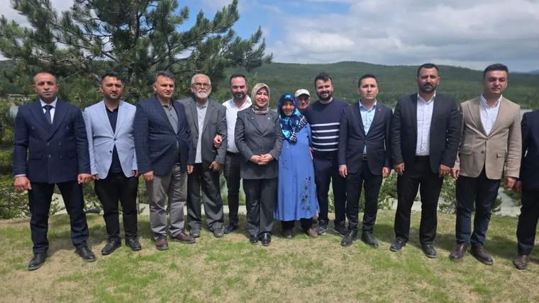 Ağaçlık tepelerin bulunduğu açık alanda, takım elbiseli ve günlük giyimli bir grup yan yana duruyor.