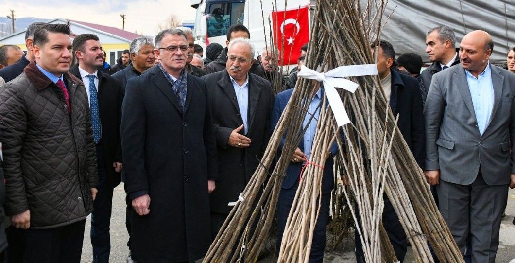 Bir grup insan, fidan dağıtım etkinliğinde bir araya gelmiş; arka planda Türk bayrağı görünmekte.