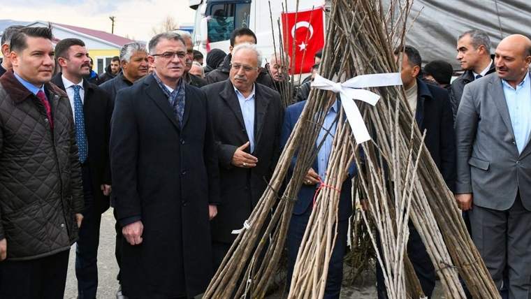 Bir grup insan, fidan dağıtım etkinliğinde bir araya gelmiş; arka planda Türk bayrağı görünmekte.