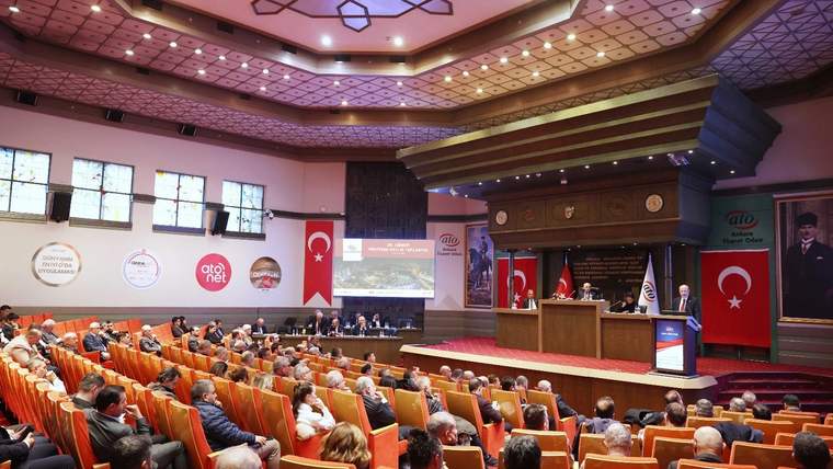 Bir toplantı salonunda, ATO Başkanı kürsüde konuşuyor, dinleyiciler dikkatle izliyor.