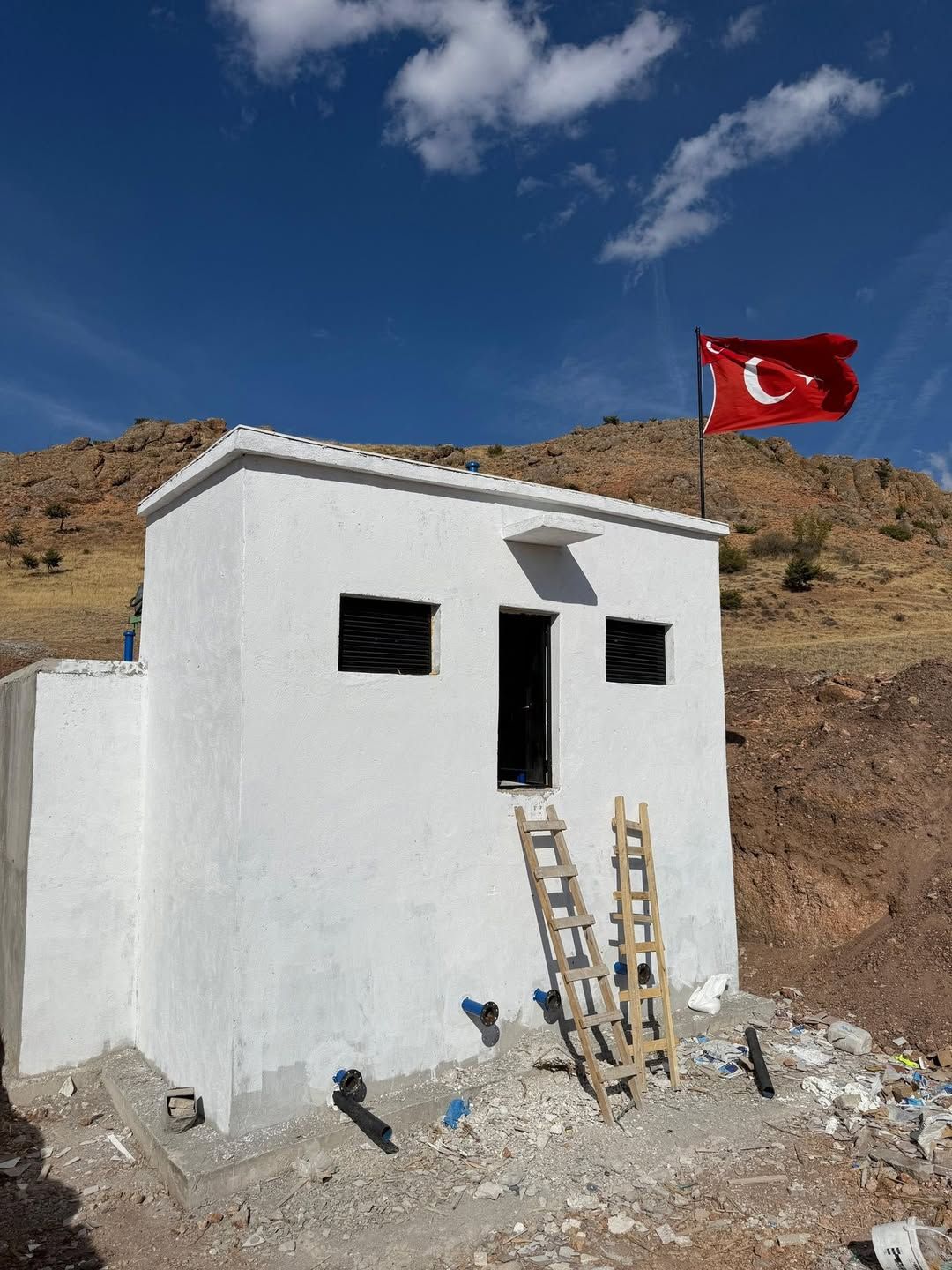 Beyaz bir su deposu, önünde merdiven ve Türk bayrağı dalgalanıyor.