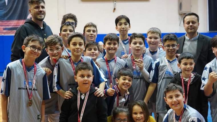 Spor salonunda madalyalı çocuklar, iki yetişkinle birlikte takım halinde kameraya bakıyor.