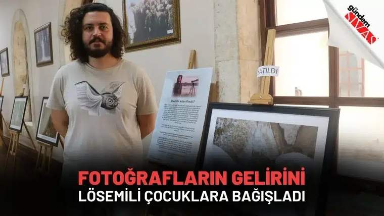 Bir adam, yanında fotoğrafların sergilendiği bir alanda duruyor.
