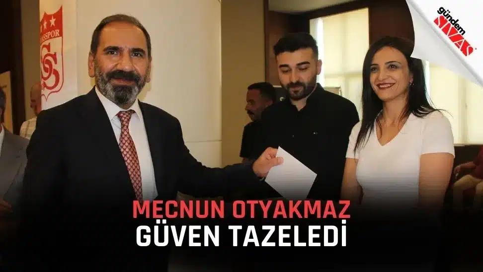 Bir kişi, elinde belge tutarak gülümseyen iki kişiyle birlikte poz veriyor.