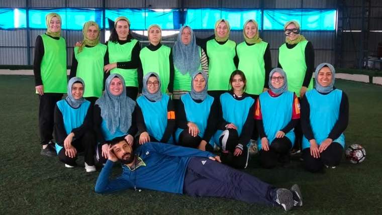 Futbol sahasında, yeşil ve mavi formalar giymiş kadın futbol takımı ve bir antrenör poz veriyor.
