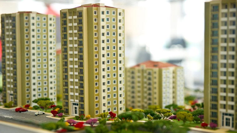 Önünde ağaçlar ve çiçekler bulunan, farklı yüksekliklerde çok katlı apartman bloklarının maketi