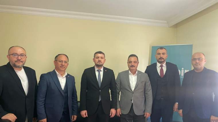Bir odada yan yana duran altı erkek, arkalarındaki mavi panonun önünde kameraya bakıyor.