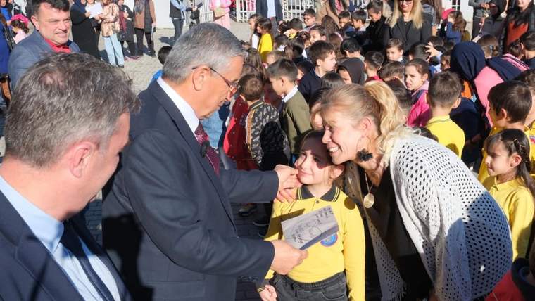 Kalabalık arasında bir çocuk, elindeki kâğıdı iki yetişkinin yanında tutarken çevresinde başka çocuklar görülüyor.