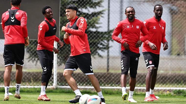 Antrenman yapan futbolcular, kırmızı formalar giymiş, gülümseyerek birbirleriyle etkileşimde bulunuyor.