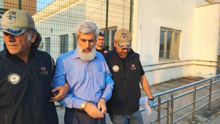 İki görevlinin kollarından tuttuğu sakallı bir adam, bina girişindeki rampada ilerliyor.
