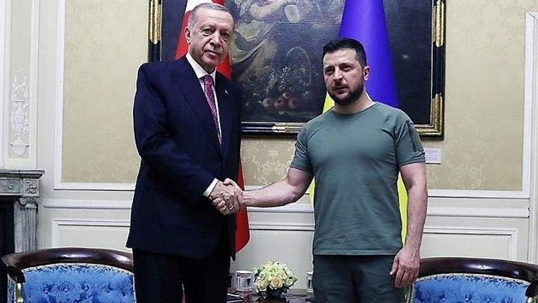 Takım elbiseli bir kişiyle tişört ve pantolon giyen kişi, bir odada el sıkışıyor.