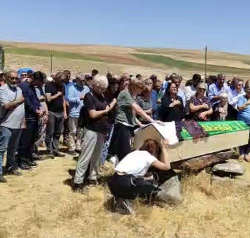 Bir grup insan, bir mezarın etrafında toplanmış, bazıları dua ediyor.