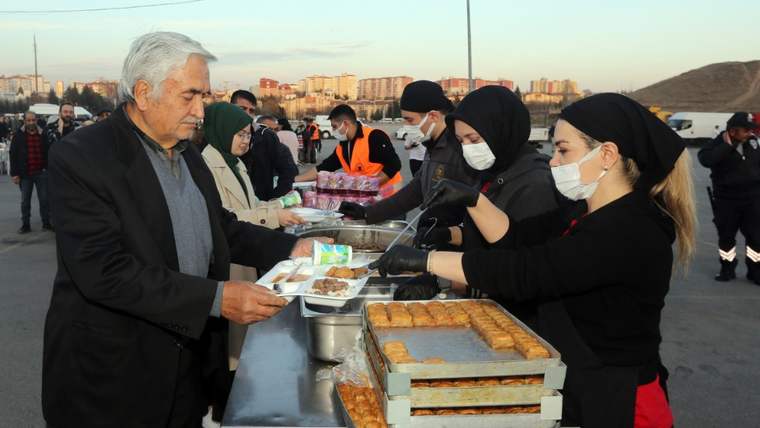 Açık alanda maskeli görevliler, tezgâhtaki yemek kaplarını uzatırken çevrede insanlar bekliyor.