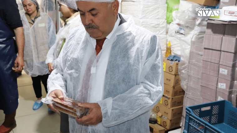 Beyaz önlük giymiş bir kişi, elinde paketlenmiş bir gıda ürünü tutuyor.