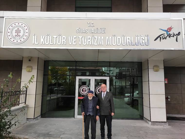 Sivas İl Kültür ve Turizm Müdürlüğü tabelası önünde, bastonlu iki kişi bina girişinde duruyor.