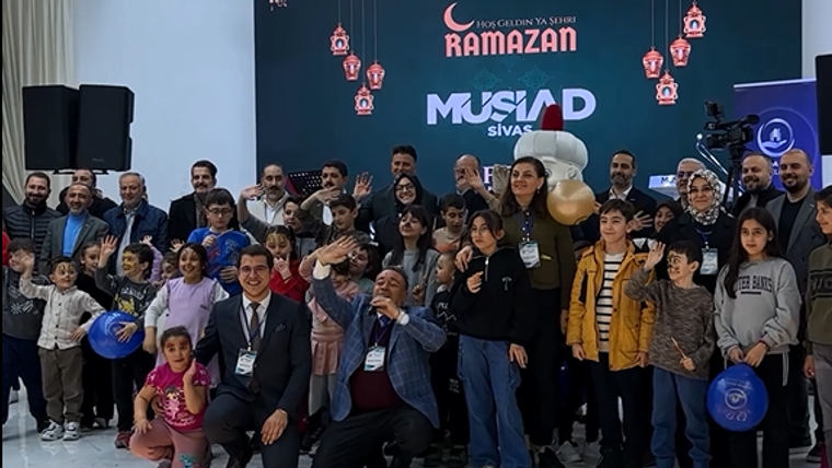 İftar etkinliğinde bir grup çocuk ve yetişkin, kameraya gülümseyerek poz veriyor.