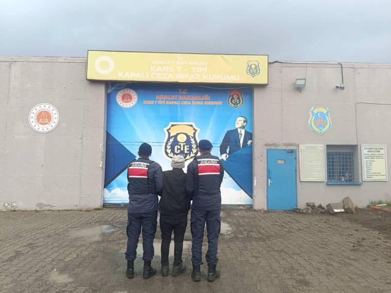 Kars T Tipi Kapalı Ceza İnfaz Kurumu tabelası önünde, arkaları dönük üç üniformalı görevli duruyor.
