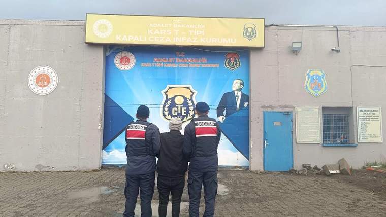 Kars T Tipi Kapalı Ceza İnfaz Kurumu tabelası önünde, arkaları dönük üç üniformalı görevli duruyor.