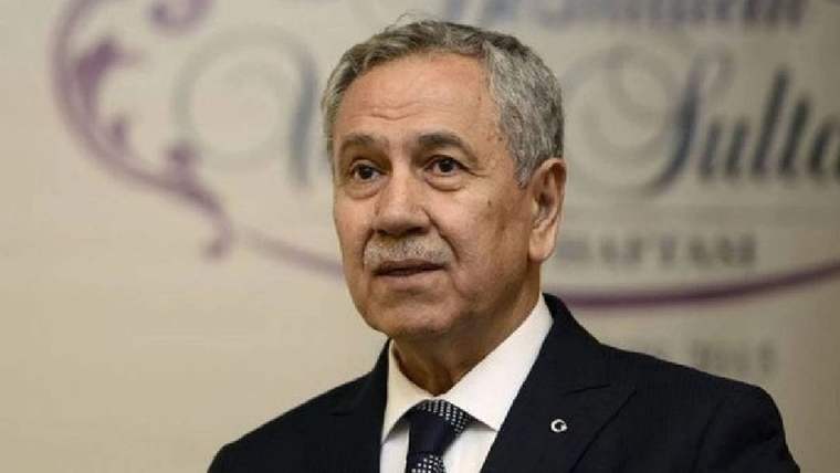 Koyu takım elbiseli, kravatlı ve yakasında rozet bulunan gri saçlı bir erkek portresi