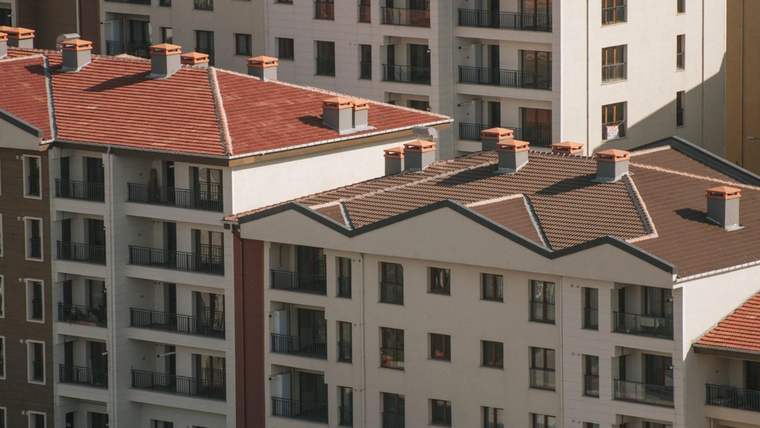 Kırmızı kiremit çatılı, çok katlı apartman binaları birbirine yakın şekilde sıralanıyor.