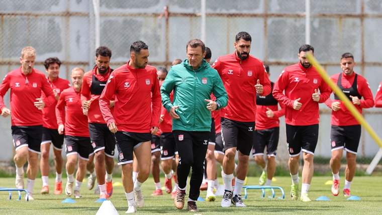 Kırmızı formalar giymiş futbolcular, antrenör eşliğinde sahada koşuyor.