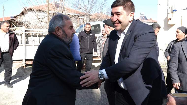 Bir kişi diğerine el sıkışırken, arka planda kalabalık bir grup insan yer alıyor.