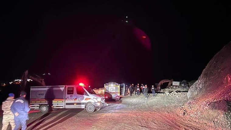 Gece, kırmızı ışıkları yanan ambulanslar ve iş makinelerinin bulunduğu kayalık alanda insanlar bekliyor.